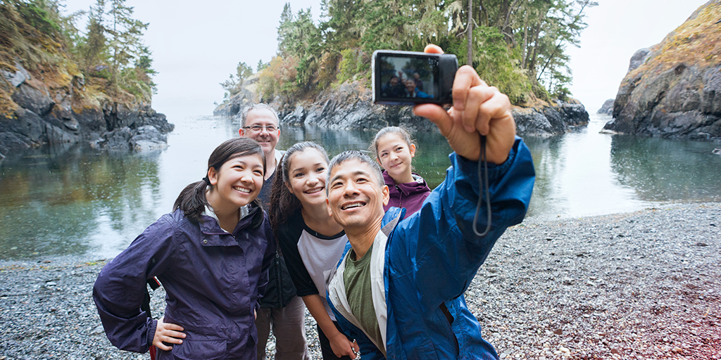 A cheerful family smiles for a beach selfie near the mountains