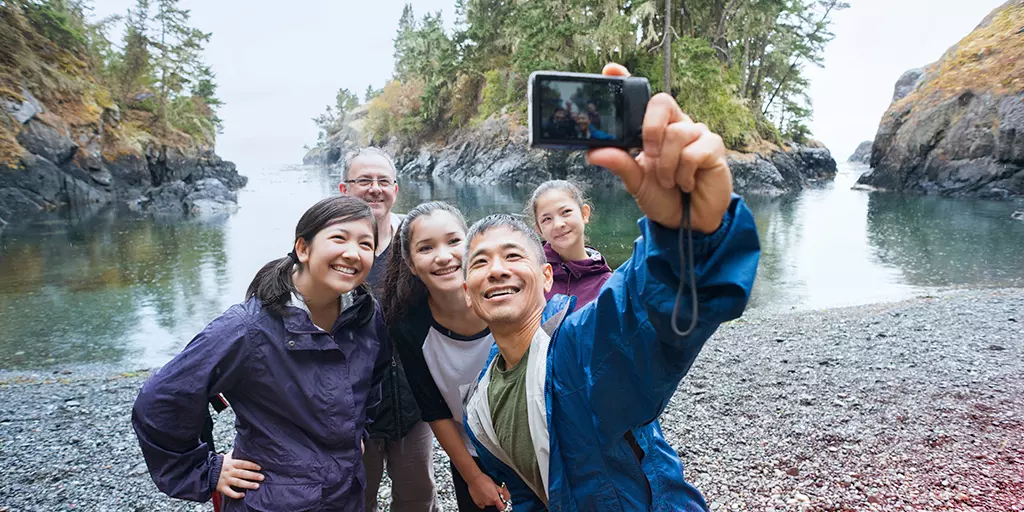 cheerful family smiles for a beach selfie near the mountains